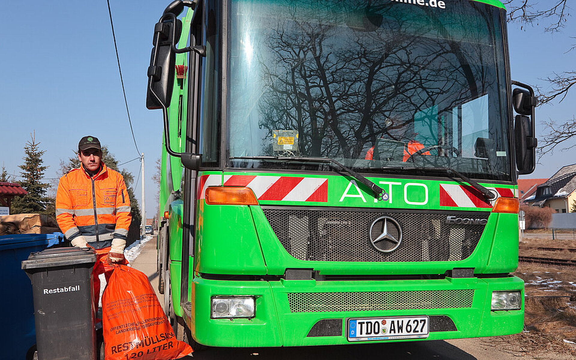 Foto zeigt Mitarbeiter der A.TO GmbH bei der Entleerung Restabfallbehälter sowie Abholung Restabfallsack